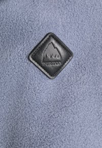 Tessuto in pile Burton di colore azzurro chiaro con superficie texture; presenta un diamante in pelle nera con un design montano e scritte in rilievo.