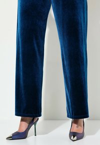 Siden navyblå bredbenta byxor som matchas med lila gradient högklackade skor med en metalisk spets och grön stiletthäl.