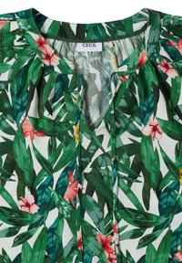 Blouse verte à feuillage avec des fleurs tropicales roses et jaunes, col rond avec liens et tissu froncé sous le col marqué "CECIL."