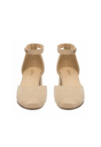 Zapatos de tacón cerrados de ante beige con tiras en el tobillo y hebillas, con un tacón de bloque de altura media y una plantilla acolchada con la etiqueta "JENNY".