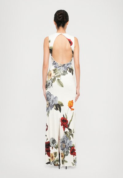 Woman with hair in a bun wearing a long white sleeveless floral dress with a large open back and zipper at the waist, standing facing away.