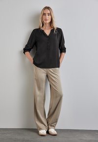 Blouse noire avec un décolleté en V et une fermeture à boutons, associée à un pantalon beige à jambes larges et des baskets blanches. Tissu doux et coupe décontractée.