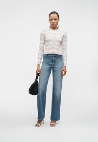 Gaiši rozā teksturēts kardigans ar pogām, apvienots ar augsto jostu ziliem taisnām biksēm. Tur rokās melnu savilkto rokassomu.