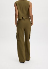 Olivgrünes, ärmelloses Cropped-Top mit einem Rückenschlitz, kombiniert mit weiten Cargo-Hosen, die über seitliche Taschen und eine glatte Textur verfügen.
