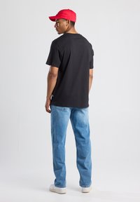 Black cotton t-shirt, relaxed fit, paired with light blue jeans and white sneakers. Red cap adds a pop of color.