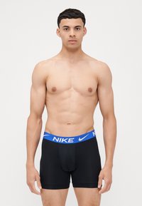 Čierne boxerky s modrým pásom s logom Nike; hladká tkanina; priliehavý dizajn; dĺžka po stredný stehno; bez ďalších vzorov alebo akcentov.