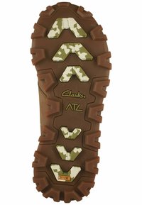 Suela de bota de senderismo de goma marrón con surcos profundos y acentos en camuflaje verde. Presenta el logo "Clarks ATL" y un acabado texturizado para un mejor agarre.