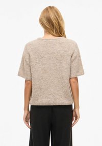 Beige kortermet genser laget av mykt, lodden materiale med rund hals. Enkel design, avslappet passform og ingen synlige lukninger.