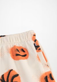 Cremefarvede shorts med et orange smiley-ansigt og basketballmotiv. Elastisk talje med syede detaljer og lille mærke på siden.