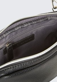 Interno di una borsa in pelle nera con chiusura a zip, dotato di una fodera in tessuto grigia e di una tasca con zip aggiuntiva, evidenziando superfici testurizzate.