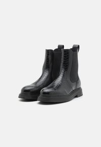 Svarta Chelsea-boots med en texturerad, präglad läderdesign, elastiska sidopaneler, dragflikar och en kraftig gummisula.