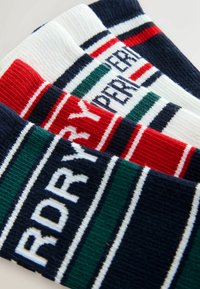 Drie paren sokken hebben een geribde textuur, met ontwerpen in marineblauw, rood, wit en groene strepen, die gedurfde tekst in contrasterende kleuren tonen.