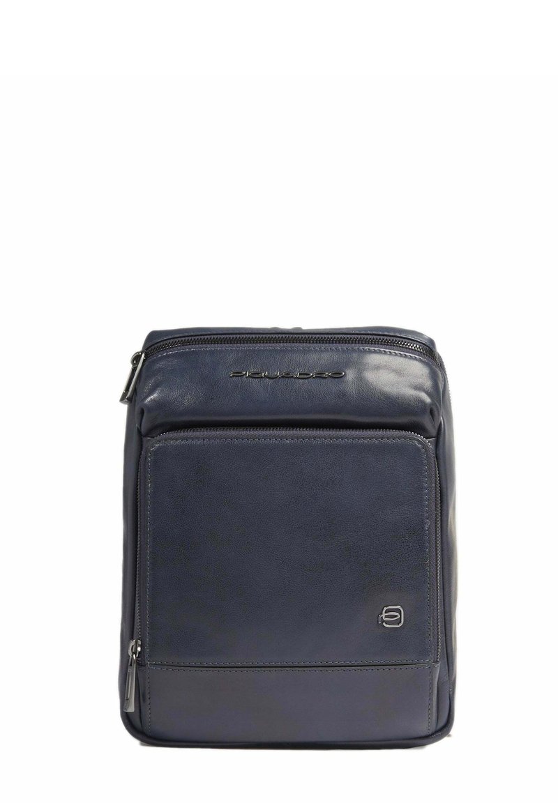 Zaino in pelle di colore blu scuro, con una texture liscia, tasca frontale con zip e accentuazione del logo sulla parte superiore. Forma rettangolare con linee pulite.