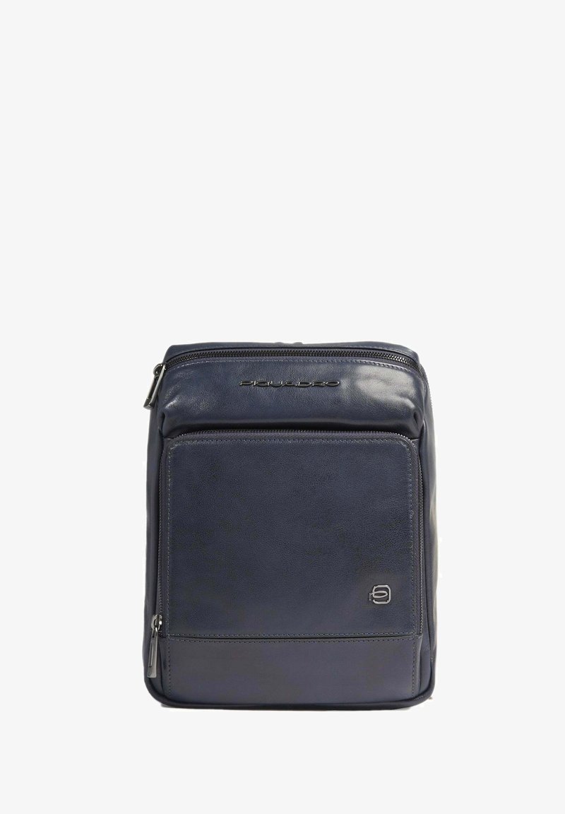 Zaino in pelle di colore blu scuro, con una texture liscia, tasca frontale con zip e accentuazione del logo sulla parte superiore. Forma rettangolare con linee pulite.