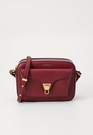 Burgundi színű bőrkistáska texturált felülettel, cipzáros záródással, arany színű fémhardverrel és elülső zsebbel, amely klipszes zárással rendelkezik.