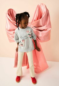 Felpa grigia chiara con il testo "È tempo di feste", caratterizzata da personaggi dei cartoni animati rossi e neri. Pantaloni a campana a coste color crema; sneakers rosse. Sfondo in raso rosa con fiocchi.