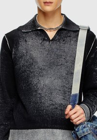 Pull noir et gris dégradé avec un col, tissu texturé et ourlet côtelé, accompagné d'un sac à épaule en denim.