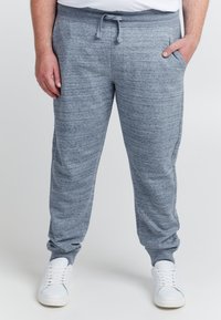 Lichtgrijze joggingsbroek gemaakt van zacht, gemêleerd materiaal, met een elastische tailleband, trekkoord en zijzakken. Gecombineerd met witte sneakers.