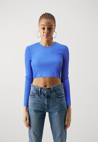 Crop top bleu côtelé à manches longues, associé à un jean taille haute bleu clair. Le tissu est lisse avec un design ajusté.