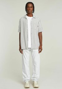 Kortærmet stribet skjorte i hvid og lys grå, parret med lyseblå jeans og beige sneakers. Har en brystlomme.