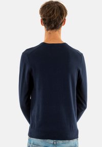 Maglione a maglia blu navy con scollo rotondo e maniche lunghe, caratterizzato da orli e polsini a costine, indossato con jeans blu chiaro.