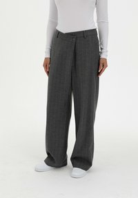 Grijze pantalon met pinstripe in een wijd model en knoopsluiting, gemaakt van textuurstof, gecombineerd met witte sneakers en een lange mouwen top.