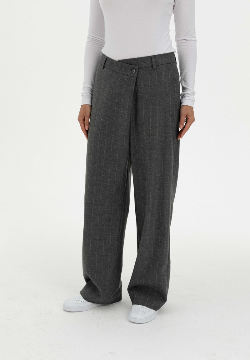 Grijze pantalon met pinstripe in een wijd model en knoopsluiting, gemaakt van textuurstof, gecombineerd met witte sneakers en een lange mouwen top.