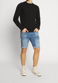 Musta kuvioitu pitkähiha-paita, vaaleansiniset käärityt farkkushortsit ja valkoiset korkeavartiset tennarit. Rentoon istuvuuteen suunniteltu rento asu.