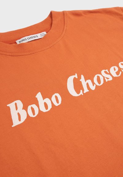 Camiseta naranja de cuello redondo con texto blanco "Bobo Choses" en el pecho y una etiqueta de talla que indica 6-7 años, 122 cm.