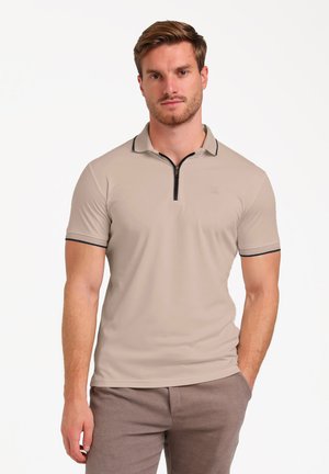 Beige poloshirt met korte mouwen en een rits aan de voorkant, met een zwarte kraagafwerking en een subtiele logopatch, gecombineerd met gestructureerde bruine broek.