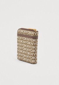 Συμπαγές καφέ πορτοφόλι με μονογράμμα με επαναλαμβανόμενο μοτίβο λογότυπου DKNY, χρυσό φερμουάρ και δερμάτινη επένδυση σε απλό ανοιχτό φόντο.