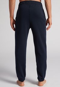 Marineblauwe sweatpants van zacht materiaal, met een elastische tailleband, zijzakken en elastische boorden bij de enkels.