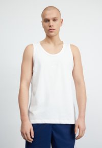 Biela bavlnená tank topka s okrúhlym výstrihom a malým reliéfnym logom Nike na hrudi. Hladká textúra, voľný strih.