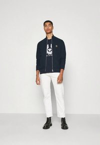 Ναυτικό μπουφάν με φερμουάρ και όρθιο γιακά, συνδυασμένο με μαύρο γραφικό t-shirt, άσπρο παντελόνι και μαύρα μποτάκια με κορδόνια. Απλός σχεδιασμός, χωρίς σχέδια.