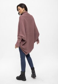 Übergroßer, gerippter Pullover in gedämpftem Mauve mit hohem Kragen, locker sitzend und mit herunterfallenden Schultern, kombiniert mit schwarzen Skinny-Jeans und schwarzen Stiefeln.