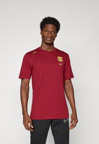 Bordo Nike t-särk lühikeste varrukatega, millel on rinnal kollane Barcelona logo ja kolm dekoratiivset nööpide õlal.