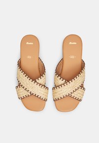 Woven natural straw sandals with a crisscross design, light tan sole, and brown stitching accents. Flat style, open-toe.