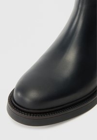 Stivale in pelle nera con punta rotonda, superficie liscia e cuciture testurizzate lungo la suola. Design semplice e resistente.