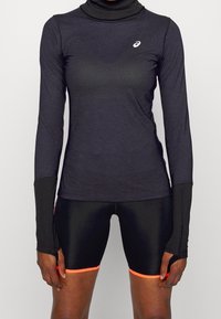 Maglietta sportiva nera a maniche lunghe con collo alto e fori per il pollice, abbinata a pantaloncini neri lucidi con rifiniture arancioni neon.
