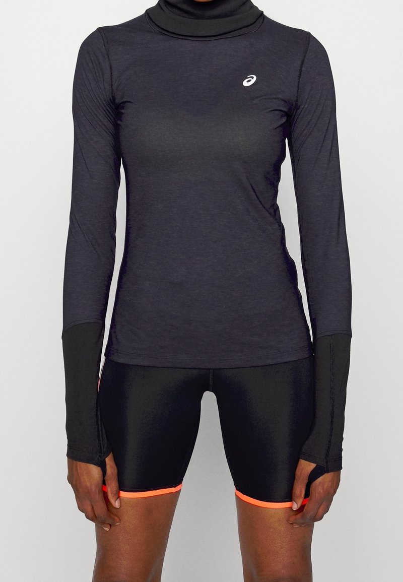 Maglietta sportiva nera a maniche lunghe con collo alto e fori per il pollice, abbinata a pantaloncini neri lucidi con rifiniture arancioni neon.