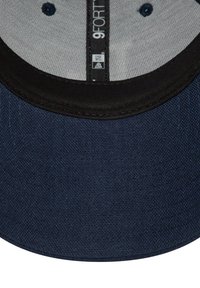 Gorra de béisbol azul oscuro con una tela texturizada, visera superior negra y parte inferior gris. Presenta la etiqueta "9FORTY" en el interior.