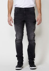 Črne denimske cargo hlače z več žepi, ožji kroj in zbledela tekstura. Imajo zadrge in dekorativne šive.