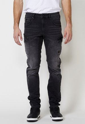 Pantalones cargo de mezclilla negra con múltiples bolsillos, un ajuste slim y una textura desgastada. Presenta cremalleras y detalles de costura decorativos.