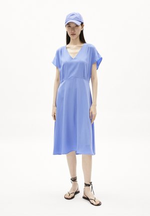 Vestido midi azul claro con mangas cortas acampanadas y escote en V. Combinado con sandalias planas negras con lazos en el tobillo y una gorra azul a juego.
