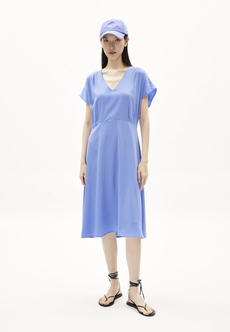 Vestido midi azul claro con mangas cortas acampanadas y escote en V. Combinado con sandalias planas negras con lazos en el tobillo y una gorra azul a juego.