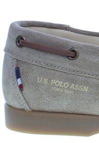 Pantofii de barcă gri din suede, cu dantelă maro și talpă din cauciuc. Prezintă detalii cu logo și un accent mic în trei culori pe lateral.