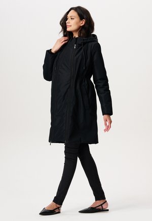 Manteau à capuche noir avec une taille élastique, fermeture éclair à l'avant et poches latérales. Tissu lisse avec une finition légèrement brillante.