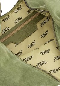 Den grønne ruskinds taske har en beige foring med et gentaget "Venezia Made in Italy" mønster og en lynlåslomme til organisering.