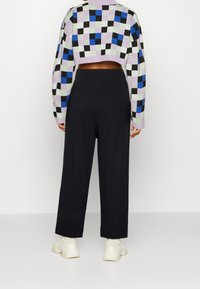 Pull court en tricot avec un motif damier violet, vert, noir et bleu. Associé à un pantalon noir taille haute à jambes larges et des baskets blanches.