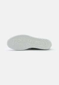 Weißer Sneaker-Sohle mit strukturiertem Grip, mit eingestanztem Logo. Kreisförmige Muster verbessern die Traktion; glatte Kanten sorgen für eine abgerundete Form.